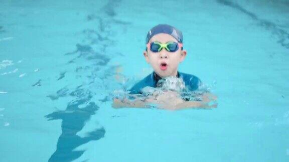 一个亚洲男孩戴着护目镜和帽子在游泳池里蛙泳夏天的假期在学校与专业人员一起学习享受和快乐的课堂运动对健康