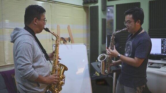 亚洲华人中年男子在音乐工作室向他的导师学习萨克斯乐器