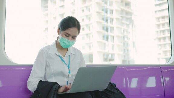 亚洲商界女性使用笔记本电脑在大规模列车上工作拥有5G互联网技术体系佩戴医用口罩防止接触冠状病毒或PM2.5粉尘在繁忙时间在户外工作