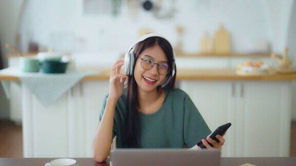 年轻的亚洲妇女戴着耳机在家里用笔记本电脑聊天在家办公视频会议在线会议视频电话虚拟会议远程学习和E-learning