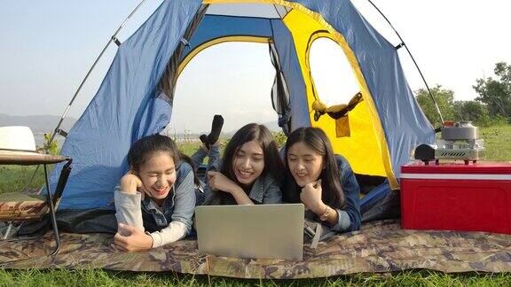 一群年轻的亚洲女孩一起在海上或湖边的旅游帐篷里使用笔记本电脑露营旅行和友谊