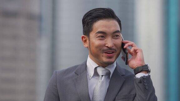 成功的亚洲华人商人在金融大楼外用智能手机交谈