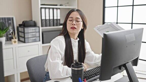 年轻的中国女商务工作者在办公室用文件当手扇