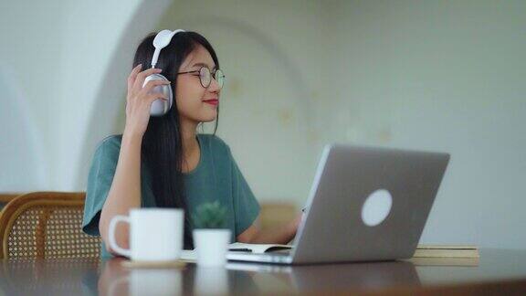 年轻的亚洲妇女在耳机交谈聊天同时使用笔记本电脑在家里在家办公视频会议在线会议视频通话虚拟会议远程学习和电子学习