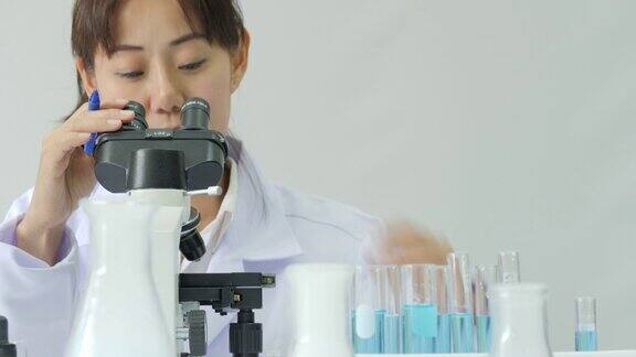 在实验室里通过显微镜观察的亚洲女性医学研究科学家