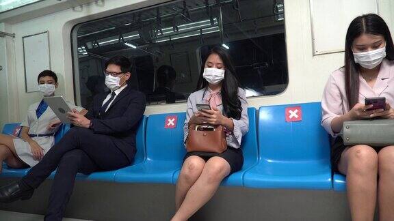 亚洲商务人士戴着医用口罩用智能手机坐在地铁里的社交距离概念新冠肺炎大流行或疫情期间的新常态