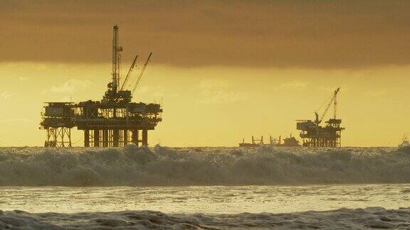 海浪撞击亨廷顿海滩海岸在南加州与几个近海石油钻井平台和石油(石油)油轮在地平线上在一个戏剧性的日落下暴风雨的天空