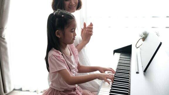 亚洲母亲和她的女儿一起弹钢琴的慢镜头母亲带着幸福和微笑拍着手教女儿