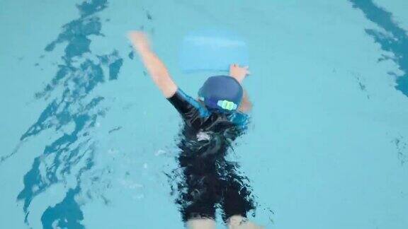 一个亚洲男孩戴着护目镜和帽子在游泳池里用泡沫自由泳夏天的假期在学校与专业人员一起学习享受和快乐的课堂运动对健康
