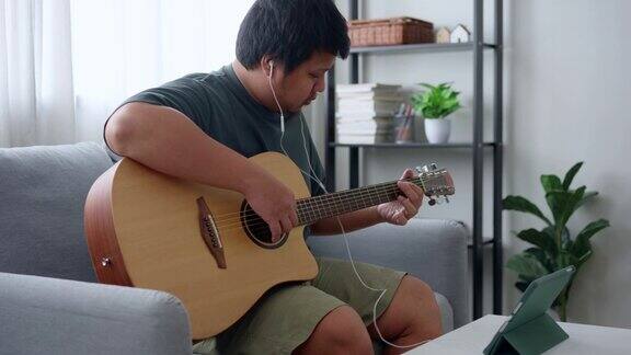 在线学习吉他亚洲男子在平板电脑上通过在线视频练习吉他