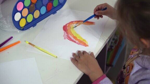 才华横溢的创意女孩女艺术家在纸上画彩虹天空夏天用手指油漆刷创造彩色孩子在家里的桌子上画画画家创作抽象现代艺术童年