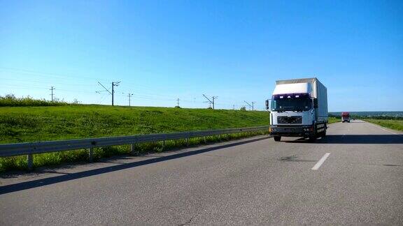 摄影机跟随卡车与货物拖车在公路上行驶在夏季的货物运输白色的卡车驶过乡村背景是美丽的风景慢镜头前视图