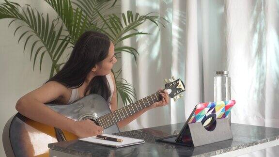 年轻的亚洲女子练习和学习如何在笔记本电脑上弹吉他