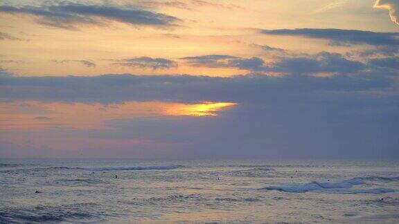 在美丽的日落时分冲浪者在蓝色的巨浪中游泳