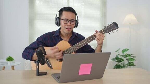 亚洲男子youtube直播表演弹吉他和唱一首歌亚洲人在网上教吉他和唱歌音乐家用笔记本电脑录制音乐演奏原声吉他