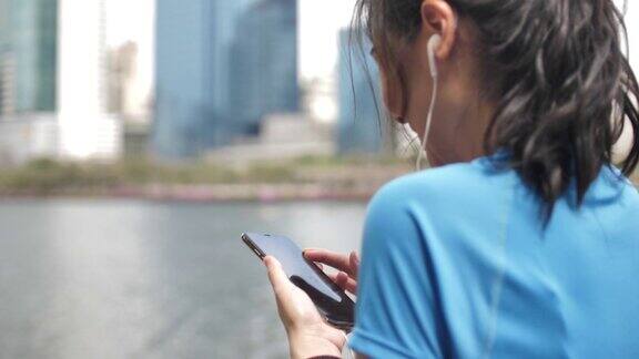 年轻的运动女性在城市里用智能手机听音乐