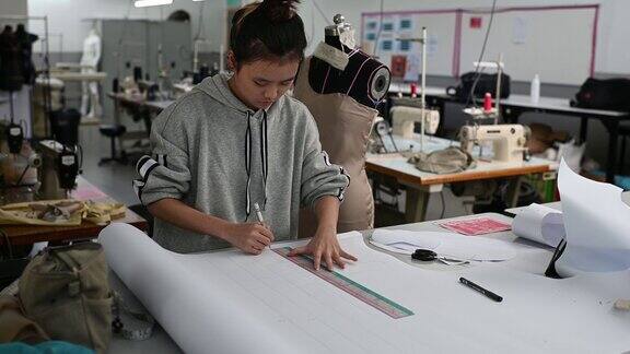 亚洲华裔女时装大学生在学院车间做服装项目写下尺寸画出缝纫图案