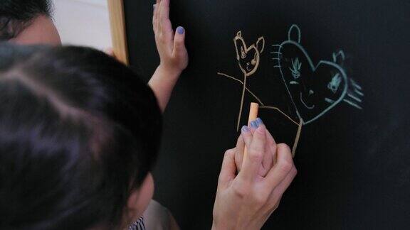 在家里客厅里快乐的母亲看着女儿在黑板上用彩色粉笔画画