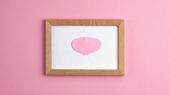 定格动画的粉红色纸心木框架在粉红色的背景在中心边情人节母亲节爱情关系浪漫的纪念日婚礼节日概念平躺