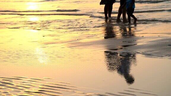 日落时分在阳光下一对夫妇带着一个小孩沿着海滩散步沿着冲浪线他们的剪影映在水中
