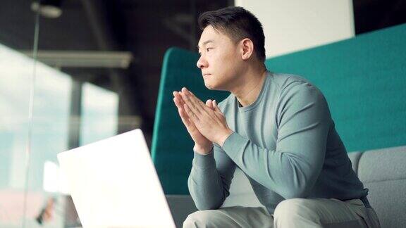 肖像有思想的年轻亚洲自由职业者在现代办公桌上用笔记本电脑工作自信专注沉思的男士室内企业家