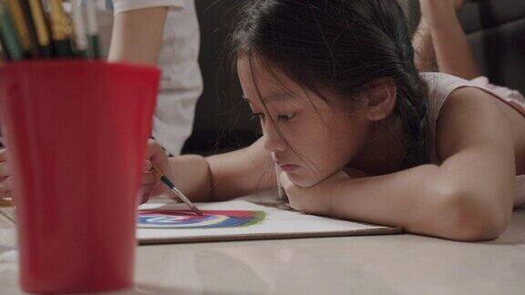 特写亚洲小女孩躺在地板上画画和绘画她的艺术和工艺在客厅而呆在家里她用水彩和画笔在白纸上创作艺术项目形成自己的想象艺术和工艺概念