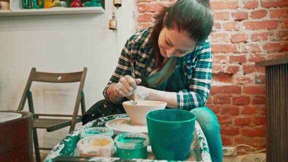 年轻女子正在用陶轮做陶器给现成的碗上釉