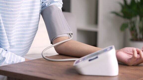 年轻的亚洲妇女在家里使用自动血压计年轻女子使用医疗设备测量血压