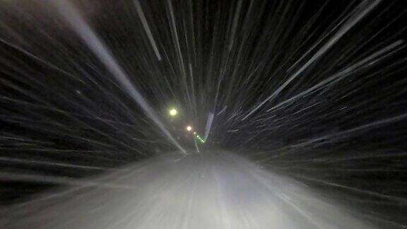 在冬天的夜晚在下雪的路上开车大雪反射着汽车前灯的光