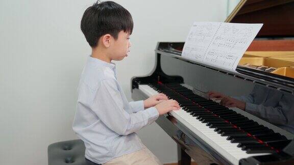 镜头从亚洲男孩在教室里弹钢琴穿着休闲衬衫的孩子孩子们在课堂上看着纸玩得开心和放松教育、技能和学习观念