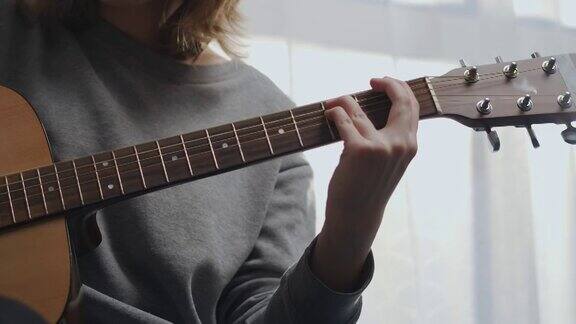 一个少年在一个白色的客厅里弹吉他房间里有美丽的阳光女人在室内作曲这位艺术家弹原声吉他女孩在练习一种乐器射击运动