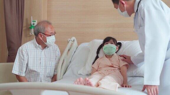亚洲男医生戴着口罩来到康复室向躺在病床上的儿童病人询问健康问题