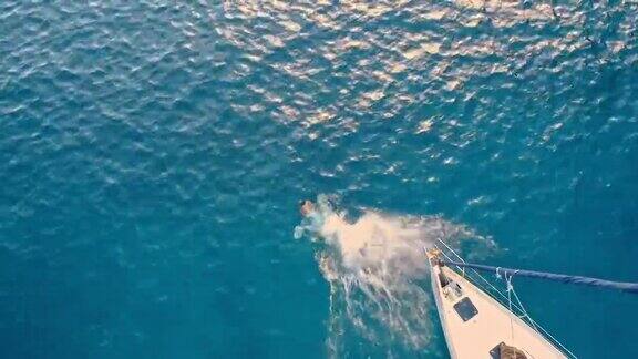 4K无人机实时拍摄男子从帆船上跳向阳光明媚的蓝色海洋