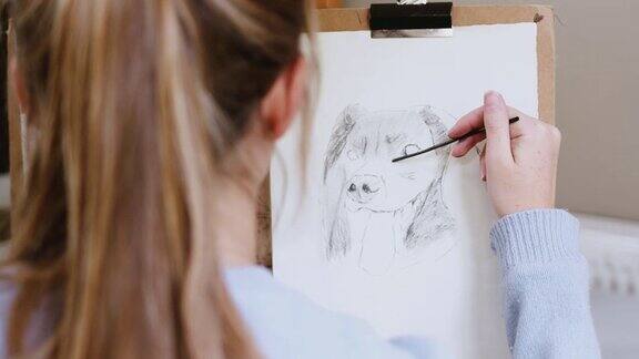 越过肩膀的女性青少年艺术家在画架上画的画在木炭狗