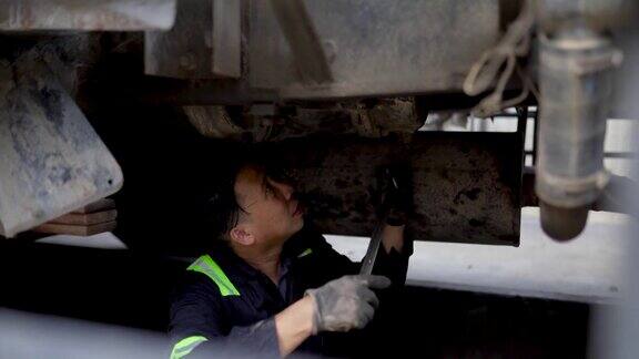 亚洲华人机械师在修理厂用扳手对卡车底盘进行检查和调整