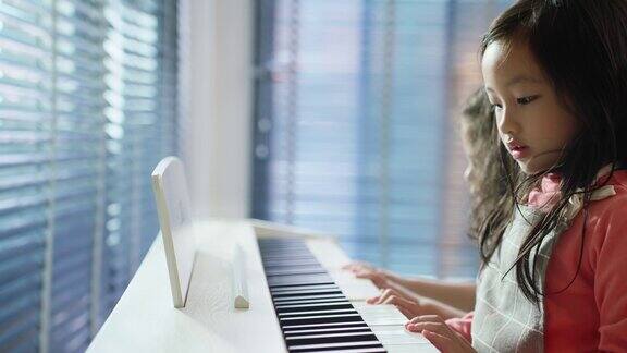 两个可爱的亚洲孩子在家里的客厅里弹钢琴年轻的小女孩们感到快乐和放松同时花空闲时间一起在教室里学习音乐
