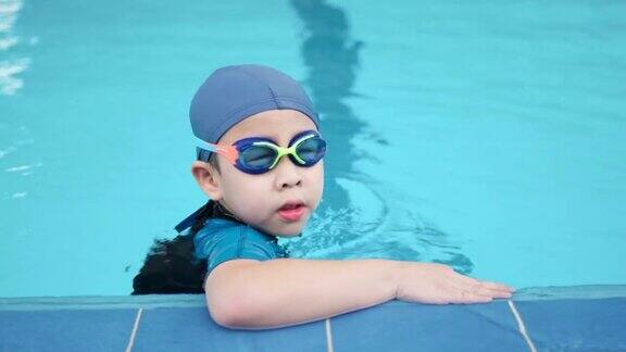 一个亚洲男孩戴着护目镜和帽子站在游泳池里转过头看着镜头夏天的假期在学校与专业人员一起学习享受和快乐的课堂