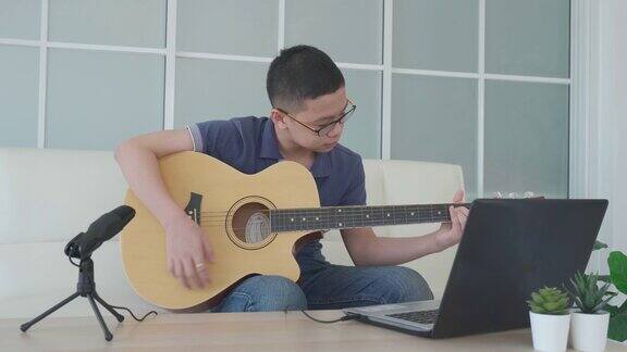 亚洲男孩弹奏吉他虚拟快乐时间会议在网上玩音乐与朋友在视频会议与笔记本电脑在网上会议在视频通话为社会距离