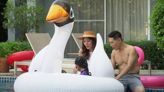 快乐的亚洲家庭带着充气或救生衣在酒店游泳池嬉戏享受夏日假期年轻的父亲和母亲女儿和儿子一起在户外游泳池放松