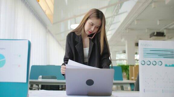 商务女性在办公室用笔记本电脑打电话处理项目文书工作