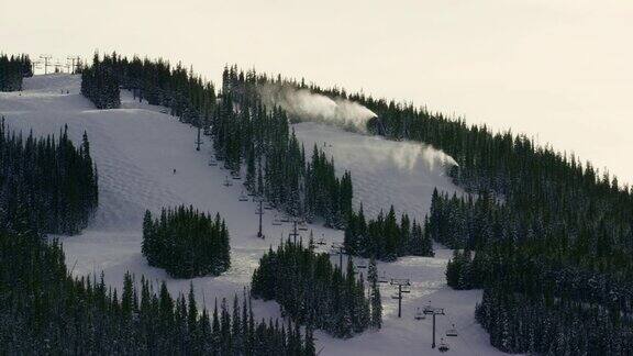 冬季日落时分在科罗拉多山滑雪度假村当人们滑雪和滑雪板滑下斜坡时雪机将雪吹到空中