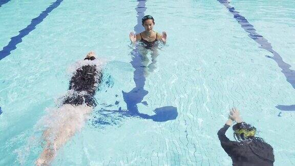 亚裔中国少年游泳运动员在游泳池里向教练练习游泳