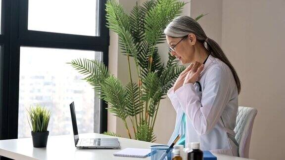 一位友善的女医生穿着医疗制服戴着眼镜在线咨询病人用笔记本电脑进行视频通话在线医疗帮助