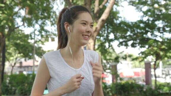 年轻迷人的女人听音乐耳机在绿色城市公园跑步健身跑步运动的人与健康的生活理念