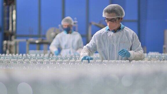 2名亚洲华人水厂生产线工人携带个人防护用品日常检查水瓶工作