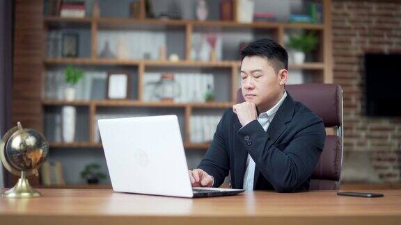 照片中有思想的亚洲商人在现代办公桌上用笔记本电脑工作自信、专注、沉思的男士在室内穿着正装