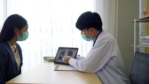 专业医生戴上外科口罩为病人讲解并展示带有肺部x光图像的屏幕笔记本电脑身穿大褂的医生在门诊病房与疑似感染冠状病毒(Covid-19)的患者交谈