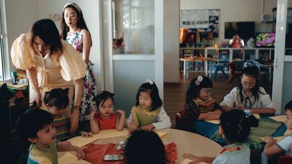亚裔华裔蒙氏幼教女老师在美术课开始前为她的学生系上围裙