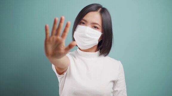 亚洲妇女戴着卫生口罩显示手停止标志孤立地站在蓝色背景卫生保健4k的视频