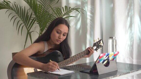 年轻女子正在玩原声吉他并观看在线吉他课程